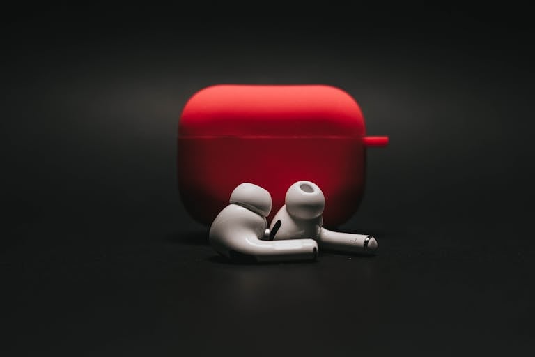 Sleek white earbuds with modern red case on a dark surface, highlighting stylish audio technology.